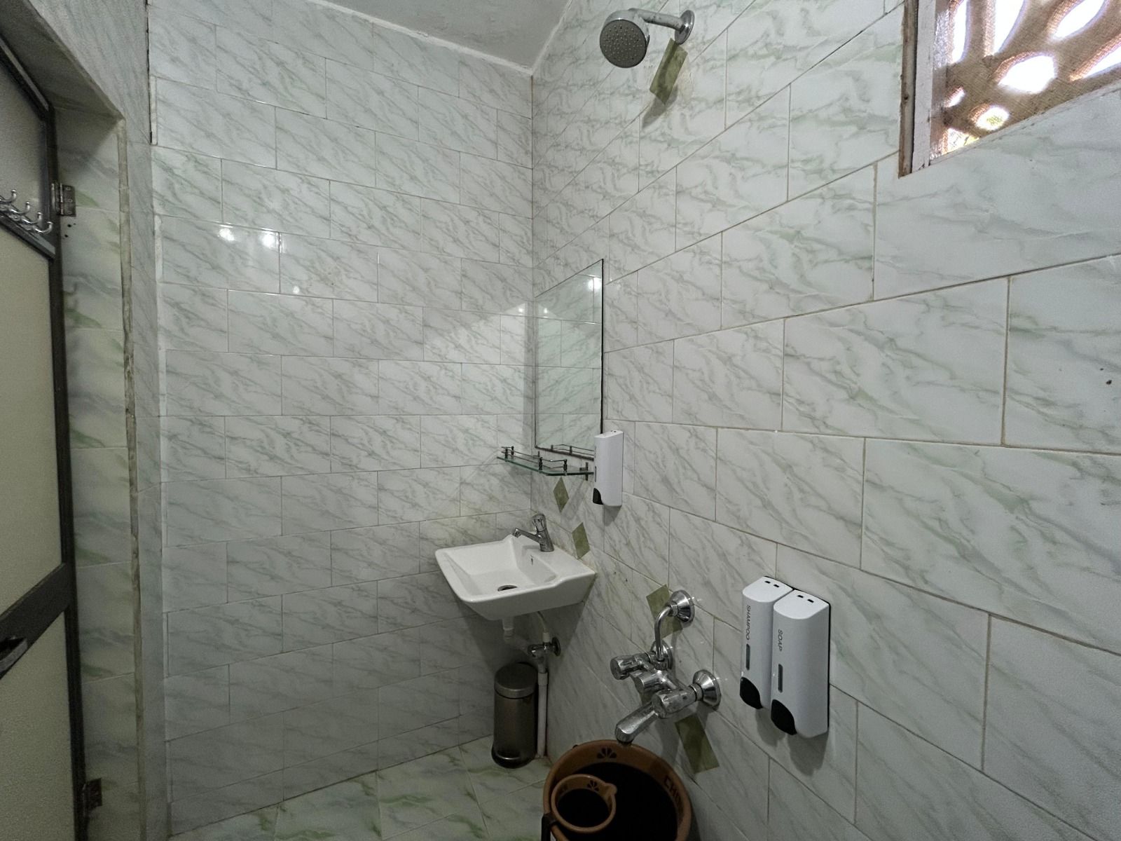 Tiled bathroom with a shower, a wash basin, a mirror and soap and shampoo dispensers